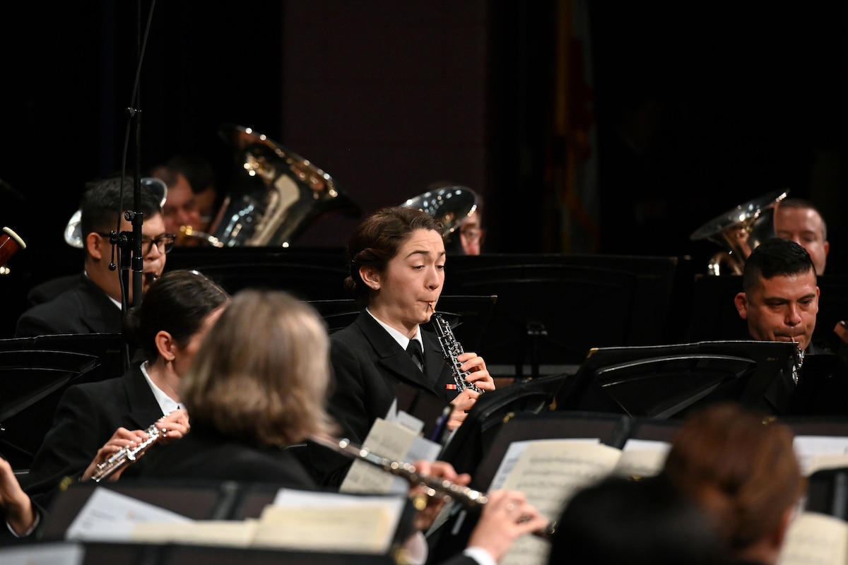 A sailor plays the clarinet among a group of sailors also playing instruments and dressed in black.