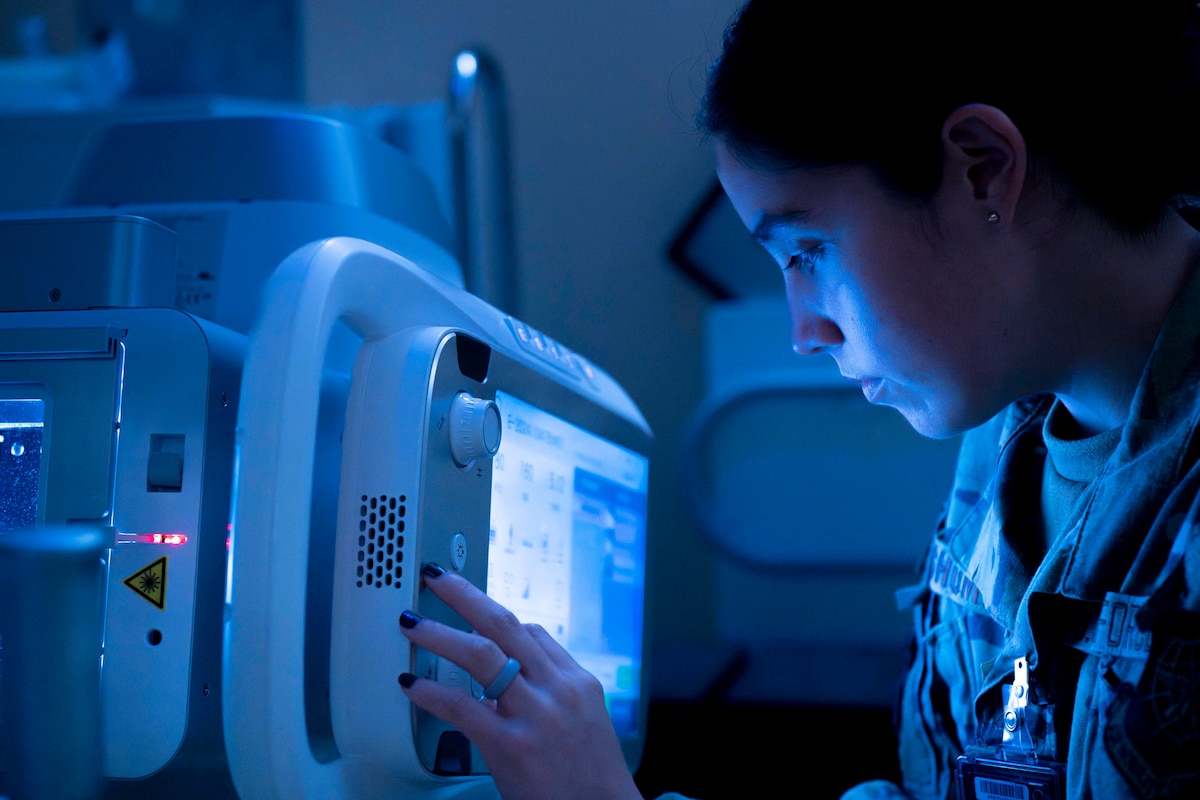 The monitor illuminates an airman’s face with blue light while they press a button on a machine.