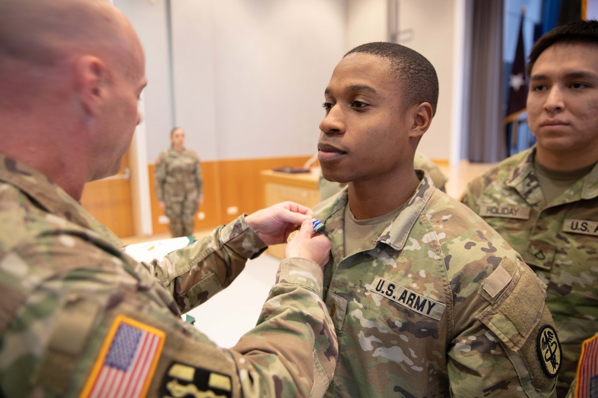 A soldier puts a pin on another soldier as a fellow soldier stands in line watching.