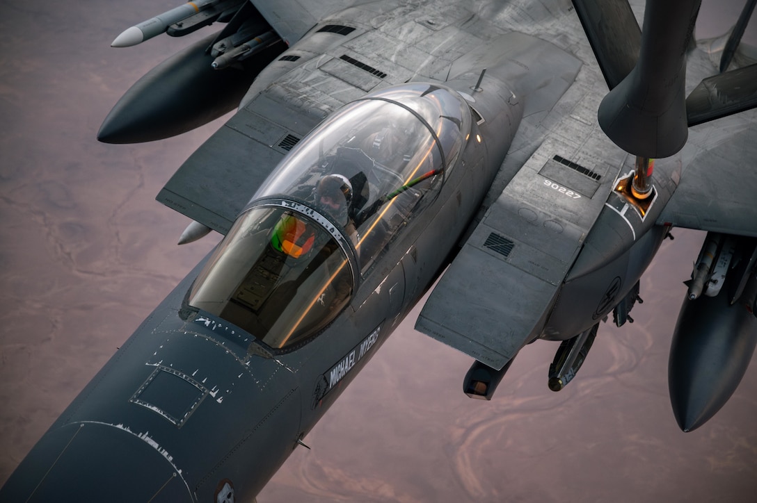 A boom is used to refuel a large plane high above brown terrain.