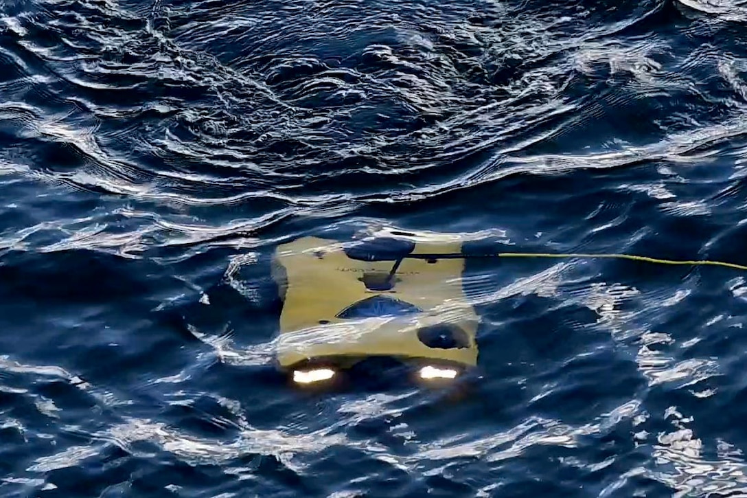 A small remotely operated yellow underwater vehicle moves just below the ocean surface while attached to a line.