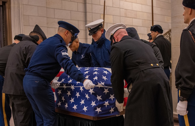 A group of service members drapes an American flag over a casket.