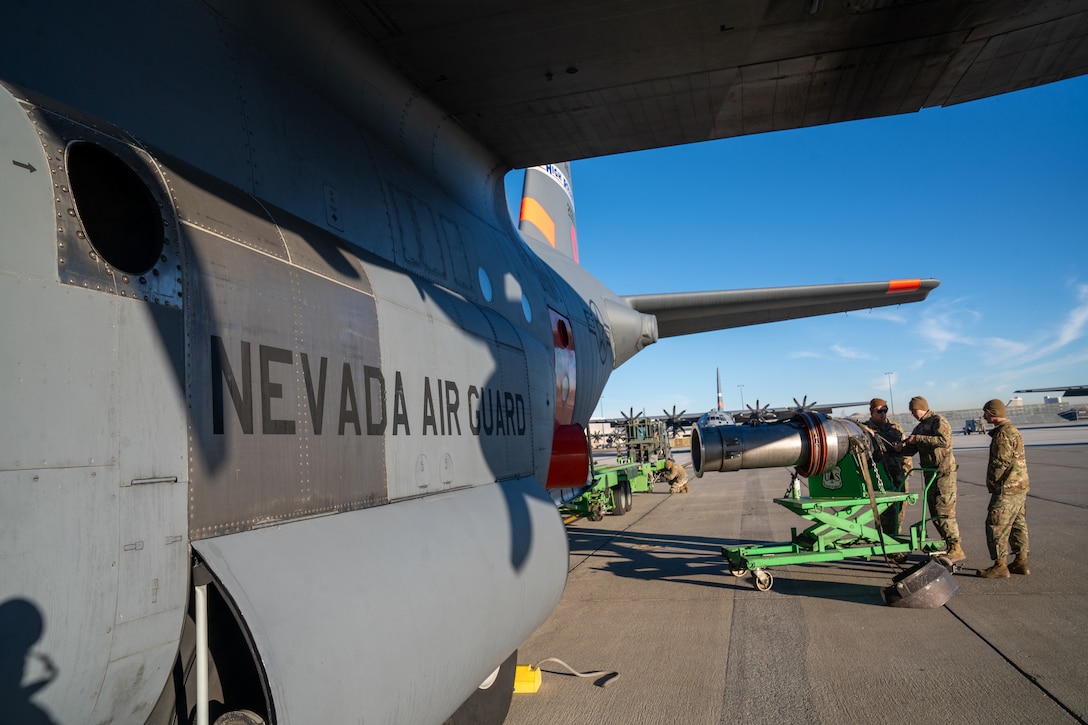 Airmen move a metal cylindrical device toward an aircraft on a flight line.