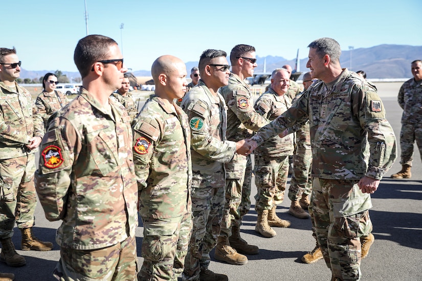 A military leader shakes hands with a line of guardsmen outdoors.