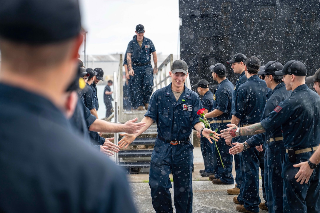 A sailor holding a rose high-fives fellow sailors lined up on opposite sides as snow falls.