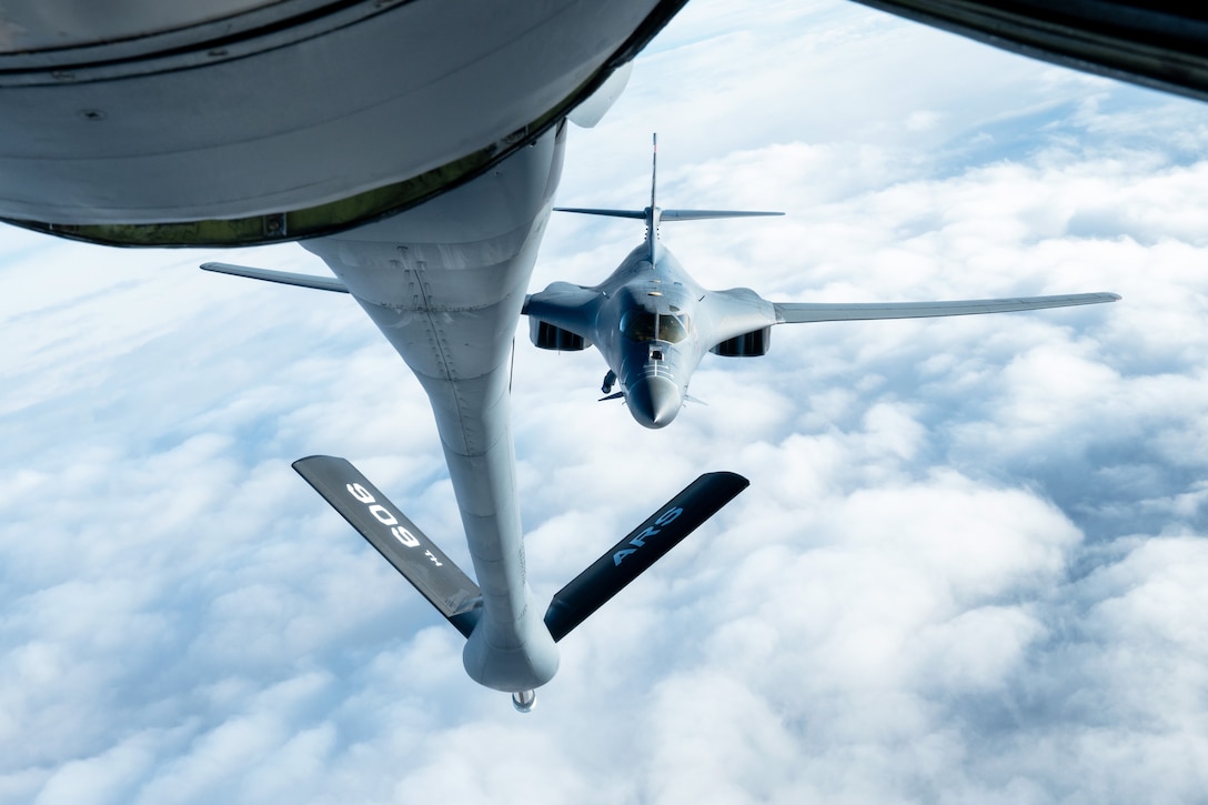 An aircraft extends its boom to an aircraft as they fly over clouds.