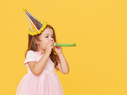 Birthday girl in a dress blowing noisemaker