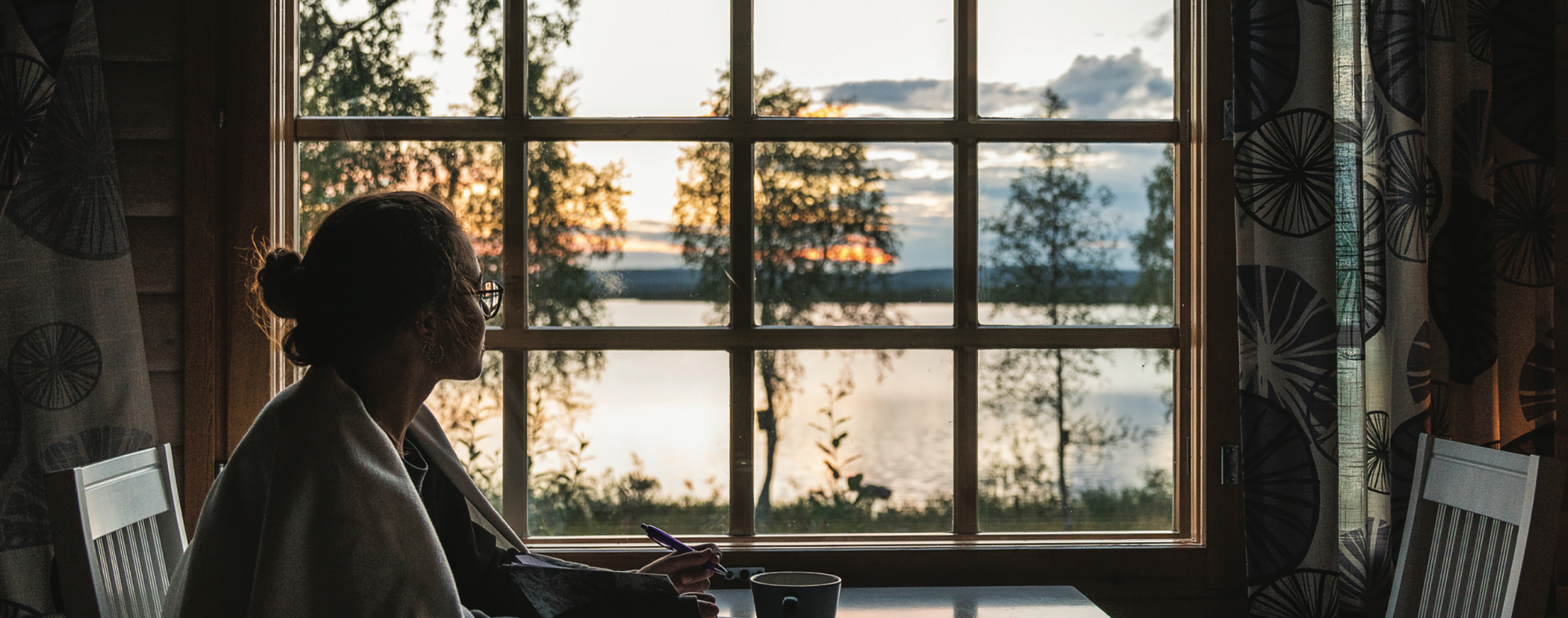 Woman gazing out window at a lake scene