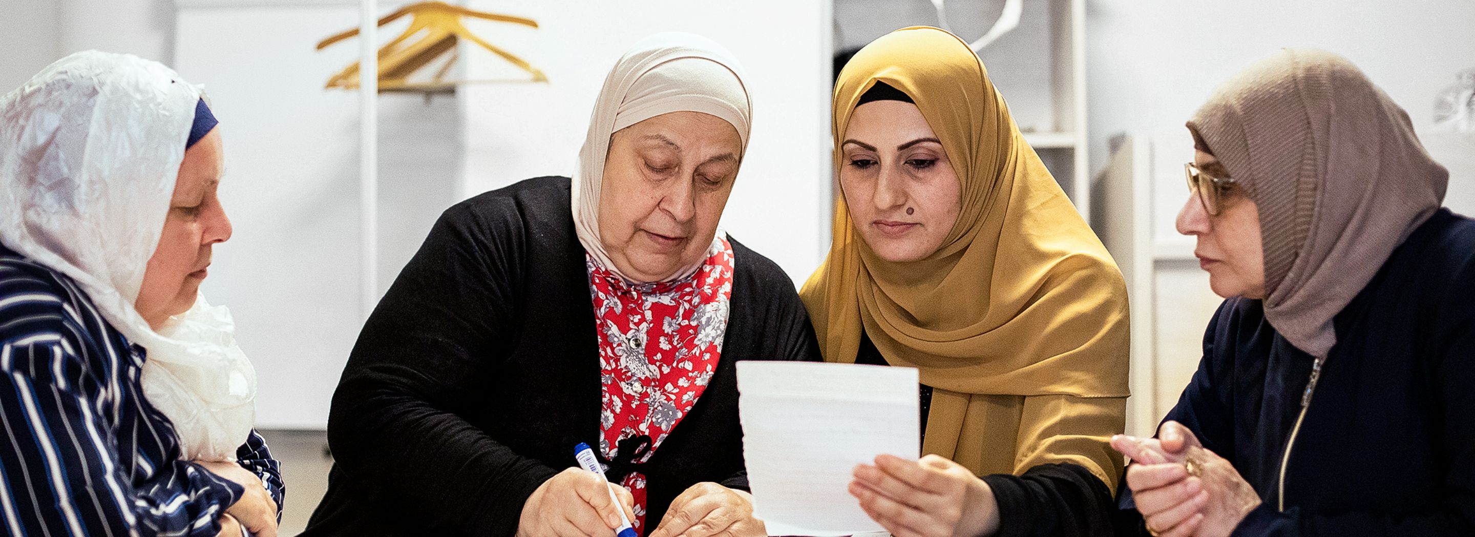 Photo: Four women wearing headscarves sitting around a table and learning together.