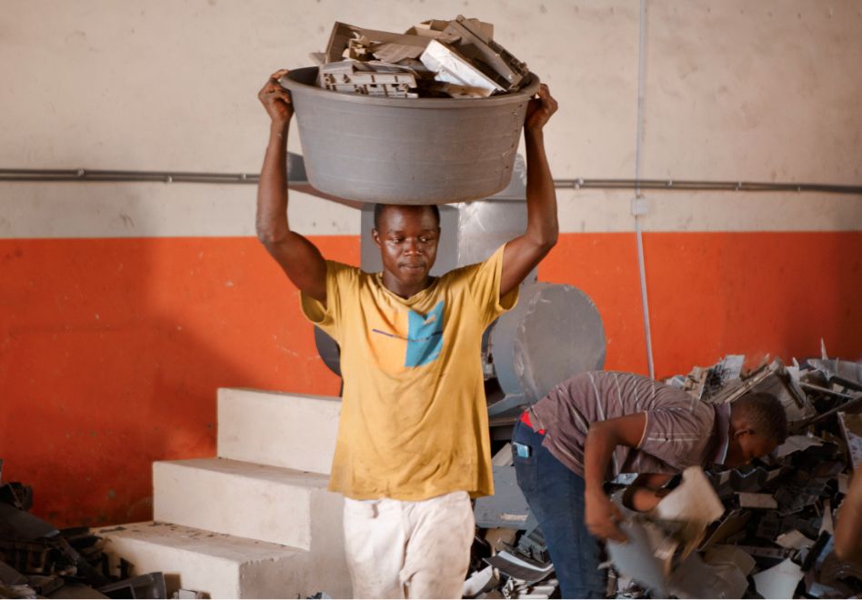 Photo: A young man carrying a plastic basin containing plastic waste on his head.