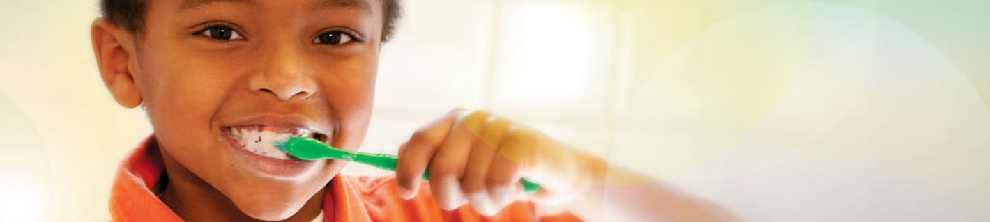 African American boy smiling and brushing his teeth with green toothbrush