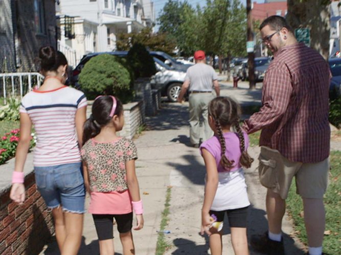 A grown-up and three children walking down the street.