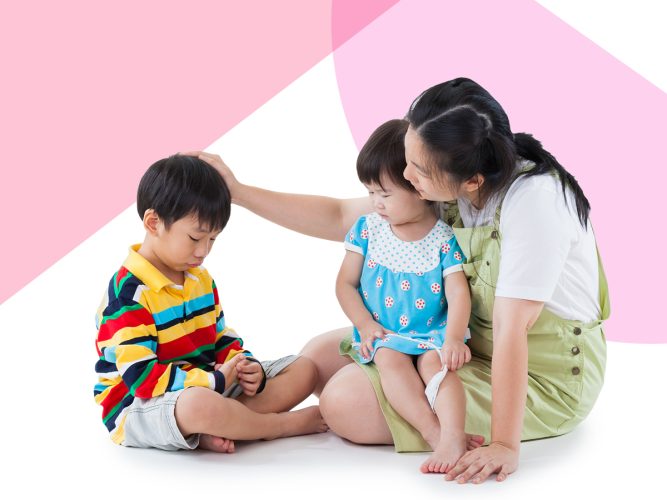 A parent with two children sitting on the ground.