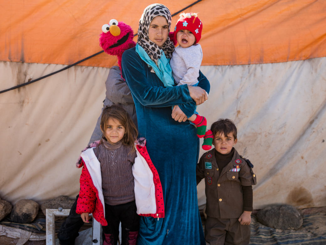 An adult holds a baby and poses with two other children and Elmo.