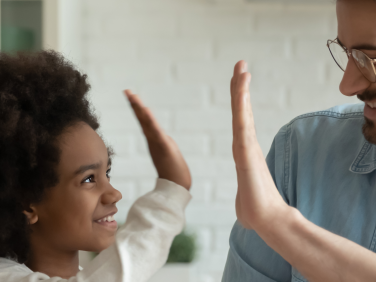 A smiling young girl high fives a father figure.