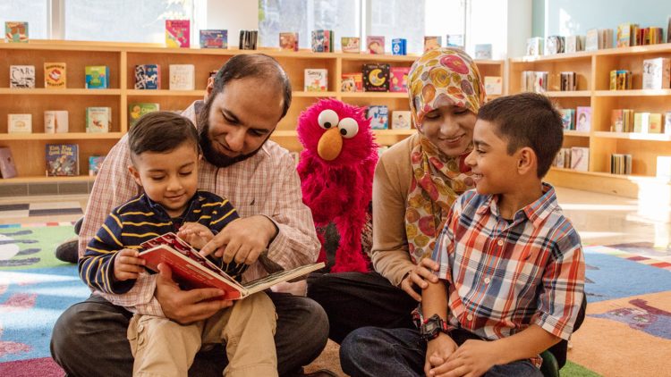 Parents reading to Elmo and their two kids in a library.