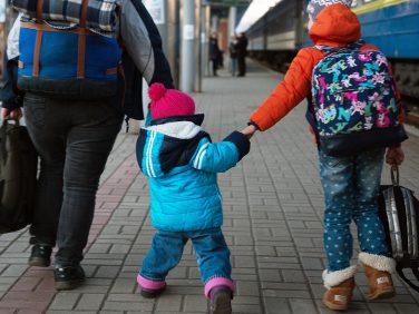 A parent with two kids walking in a train station depot.