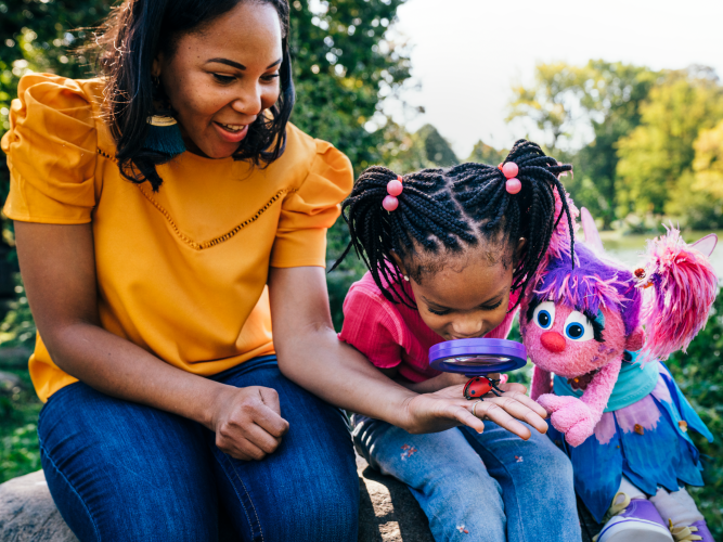 A chid uses a magnifying glass with Abby Cadabby and her mother.