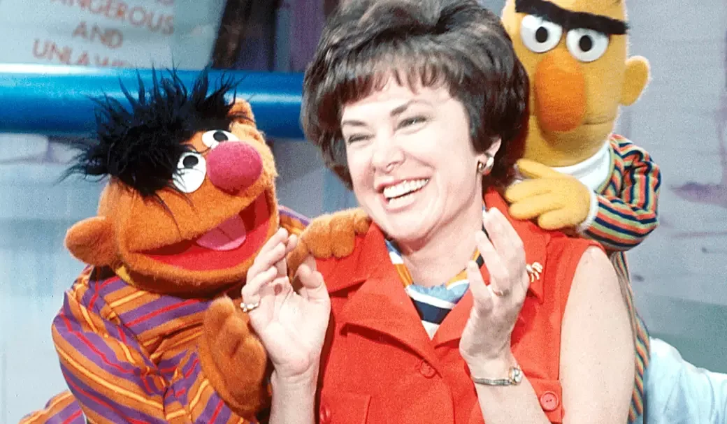 Joan Ganz laughing as Bert and Ernie sit on her shoulders.