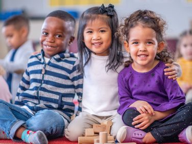 Three young kids smiling and playing with blocks in class.