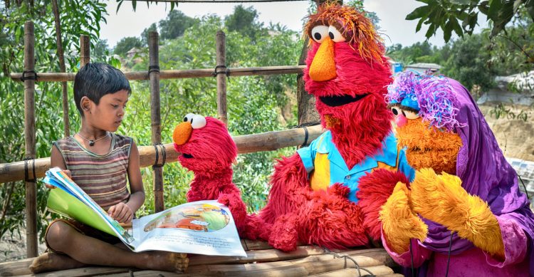 Elmo, Louie, and Mae reading with a child.