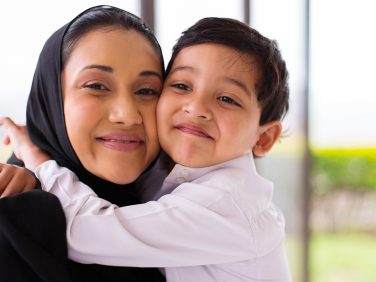 Mother and Son hug each other and smile into camera.