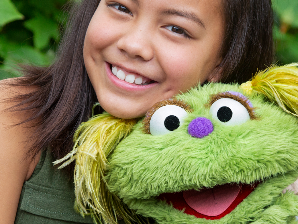 A little girl sitting on a park bench with the Sesame Street character Karli.