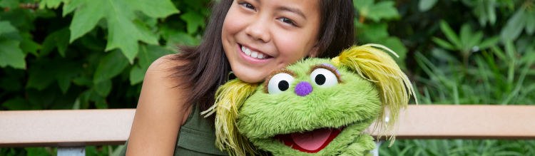 A little girl sitting on a park bench with the Sesame Street character Karli.