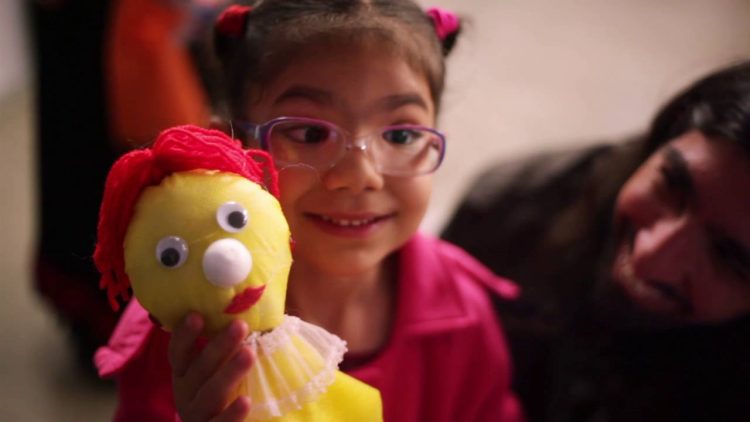 A young child holds up a puppet they crafted