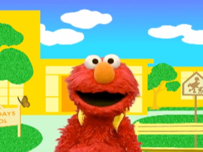 Elmo poses in front of a school wearing a backpack.