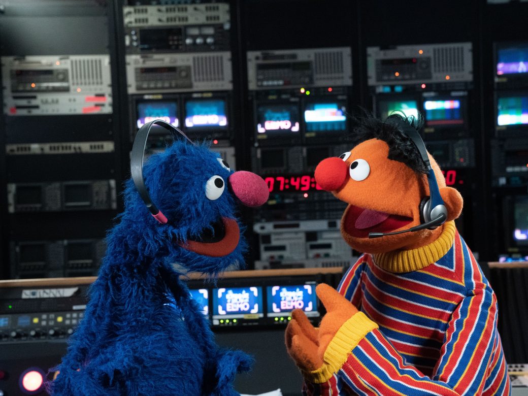 Ernie and Grover smile at each other wearing headsets backstage