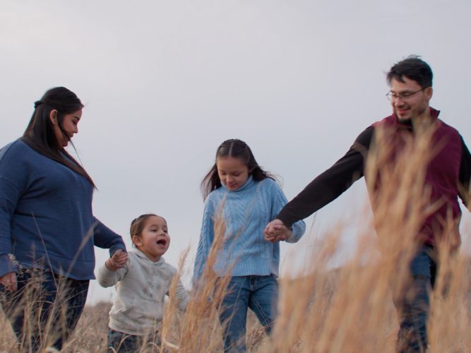 A family walks through a field holding hands.