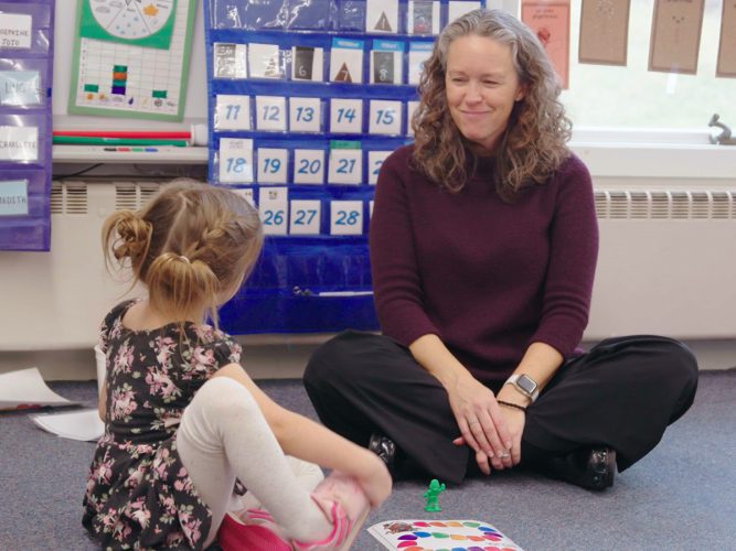 A teacher smiles at a student as they play a game