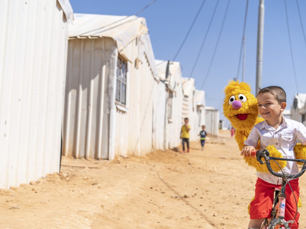 A boy riding a bike with a muppet in the middle east.