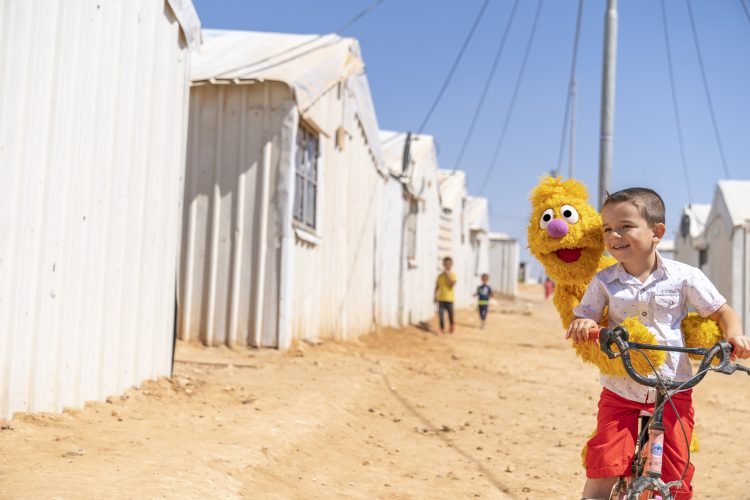 A boy riding a bike with a muppet in the middle east.