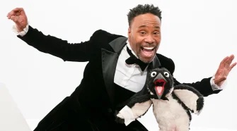 Billy Porter, dressed in a tuxedo, dances with a muppet penguin.