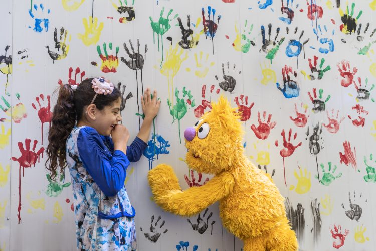 Jad and a young girl pose against a mural of colorful handprints.