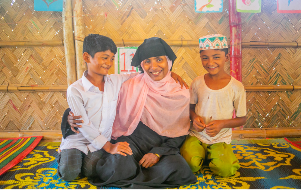 Two children pose happily with a supportive adult.