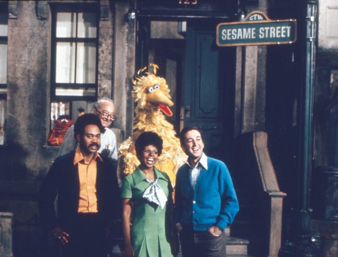 Gordon, Susan, Bob, Mr. Hooper, and Big Bird pose on the stoop of Sesame Street