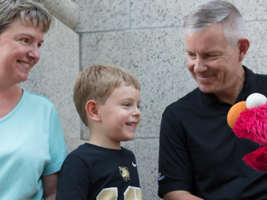 A young boy plays on a tablet with his parents and with Elmo.