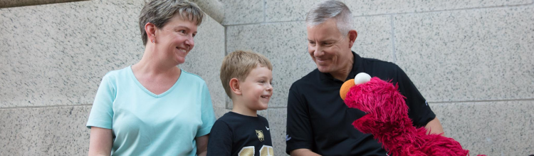 A young boy plays on a tablet with his parents and with Elmo.