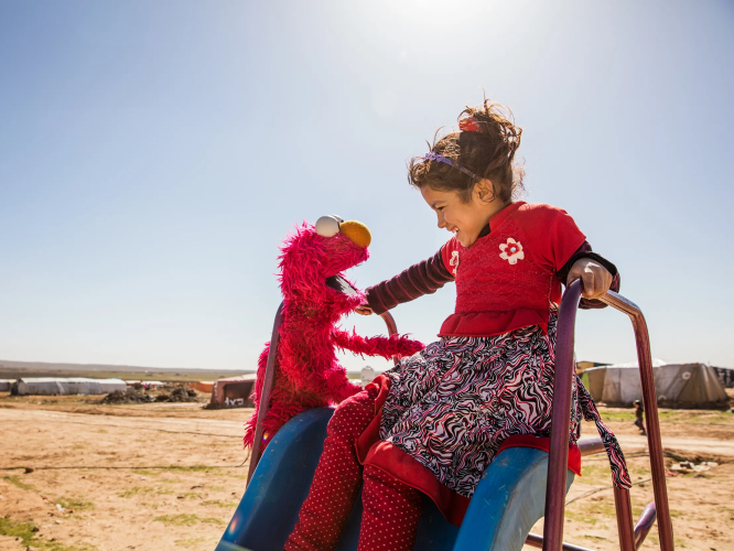 Elmo playing with a child on a slide.