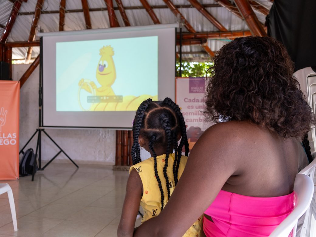 Mother and child watching Jad on a projector screen.