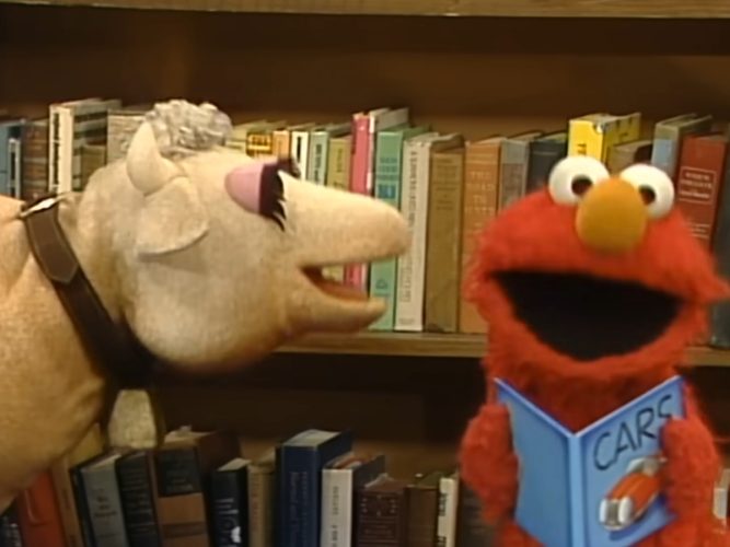 Elmo and a cow in the library.