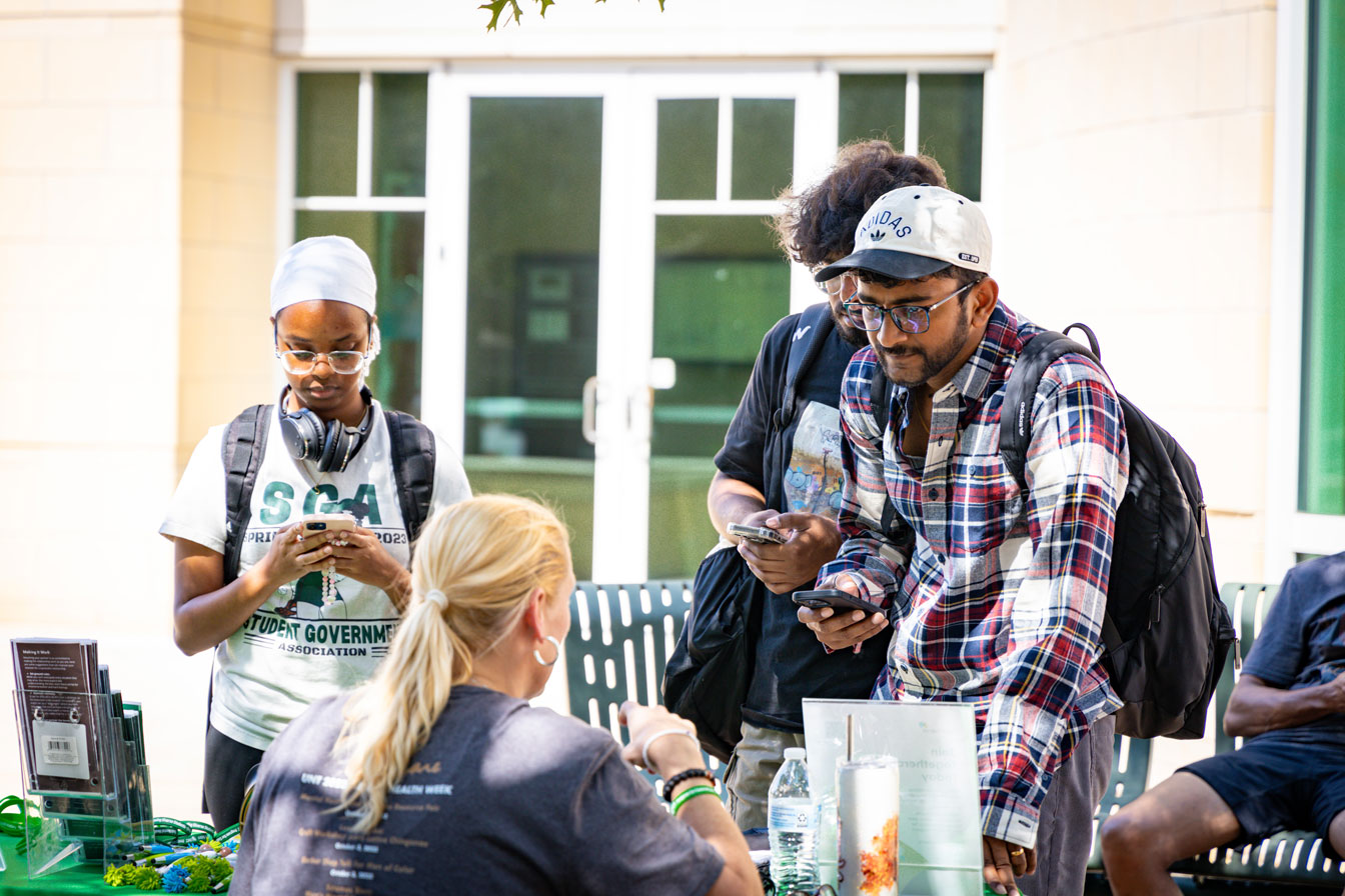 students inquire about the services offered by counseling and testing at a table outdoors with handouts littered on the surface.