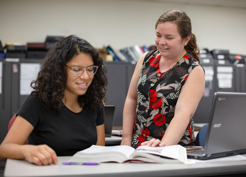 Two women consider the text in a book.