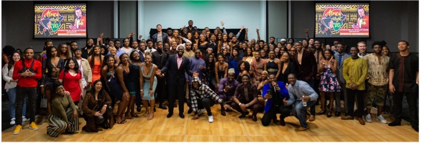 A large group of students pose in front of designs that incorporate the outline of the African continent.