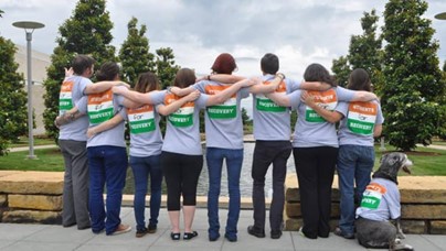 Students gathered arm-in-arm at the edge of a reflecting pool.