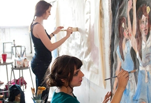 two girls painting on paper pinned to wall