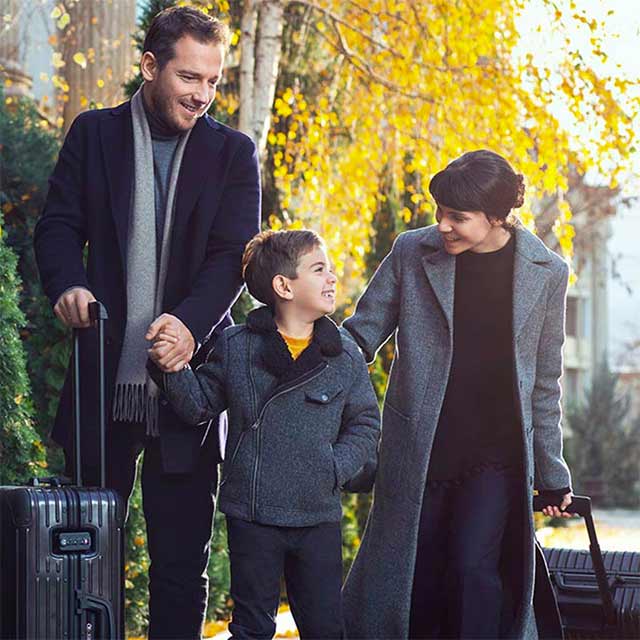 A man and a woman stroll outside with their son while dragging suitcases.